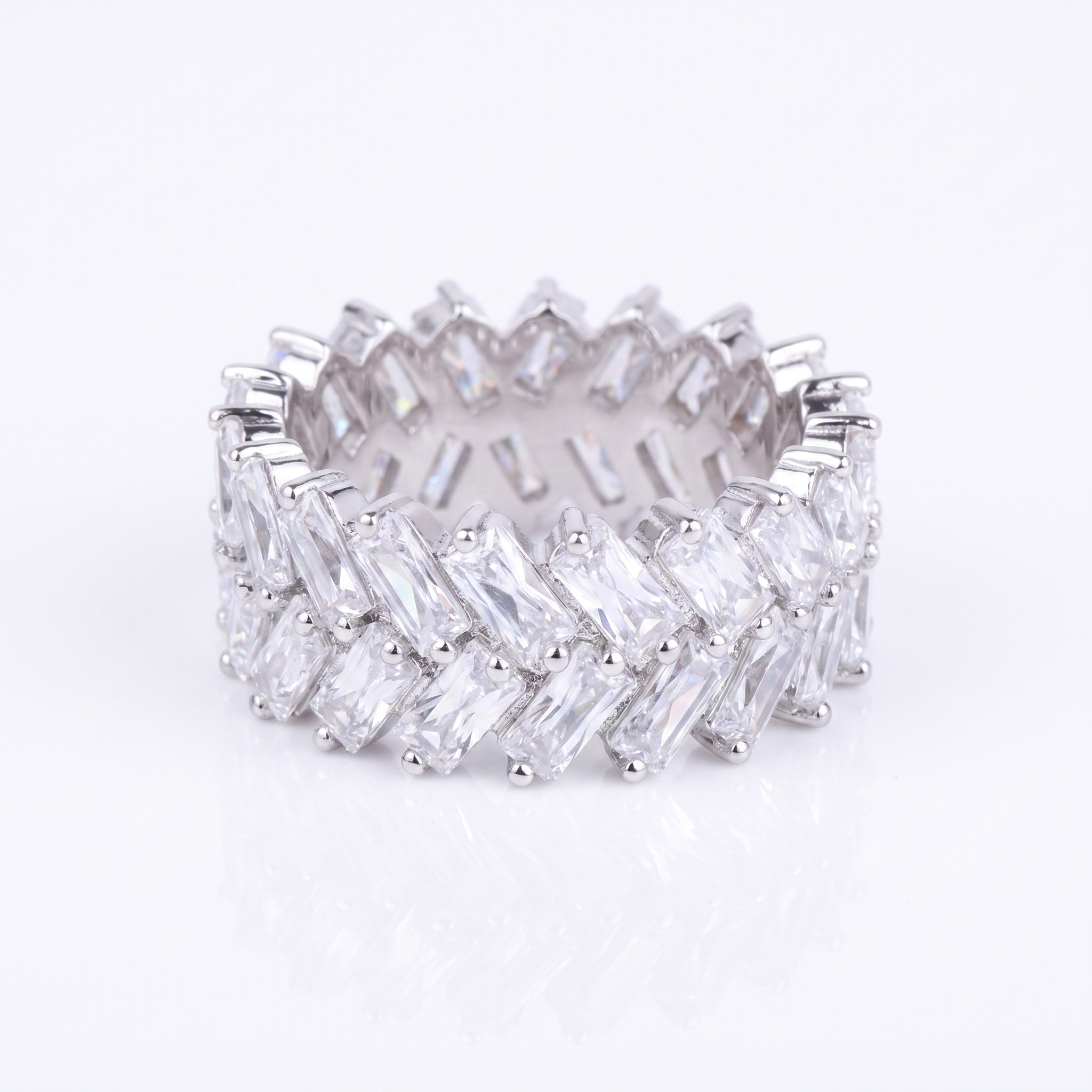 A silver-toned eternity band ring set with multiple rows of clear baguette-cut gemstones, photographed on a clean white background with a soft reflection below.