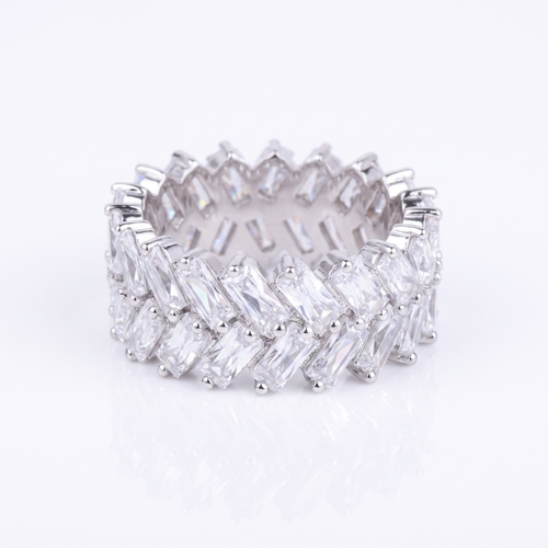 A silver-toned eternity band ring set with multiple rows of clear baguette-cut gemstones, photographed on a clean white background with a soft reflection below.